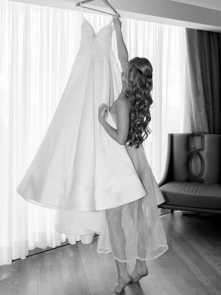 Bride adjusting her wedding gown hanging by the window during bridal preparations at Divani Apollon Palace and Thalasso