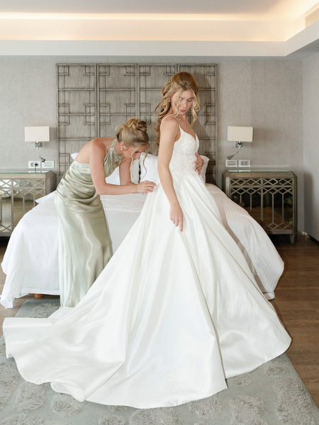 Bridesmaid fastening bride’s gown during luxury wedding morning at Divani Apollon Palace and Thalasso