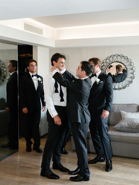 Groomsmen helping groom adjust bow tie during luxury wedding preparations in Athens