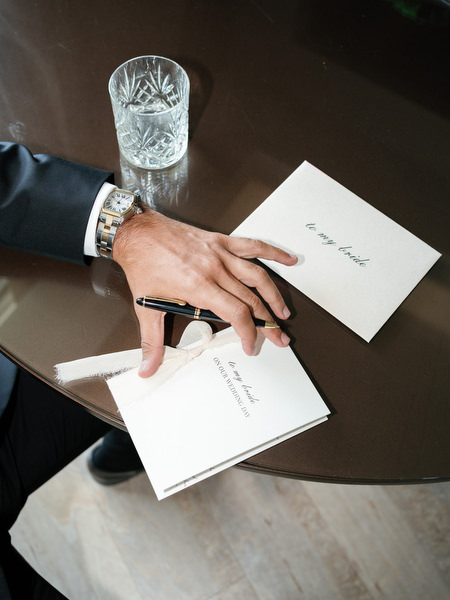 Close-up of groom’s hand holding wedding stationery and vow letters during Island Resort Athens Riviera wedding