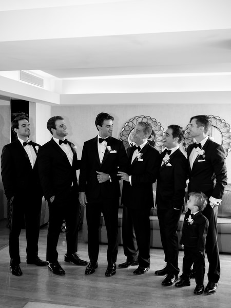 Groom and groomsmen in black tuxedos posing together during Island Resort Athens Riviera wedding morning