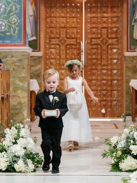Ring bearer and flower girl walking down aisle during Orthodox wedding ceremony in Athens
