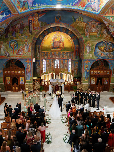 Wide view of Greek Orthodox wedding ceremony inside ornate Athens church with colorful frescoes