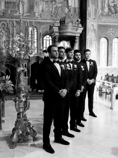 Groomsmen standing inside ornate Greek Orthodox church before ceremony in Athens