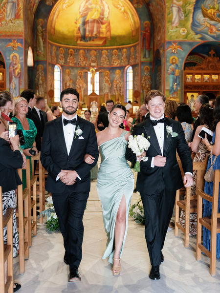 Bridesmaid in sage green gown walking arm in arm with groomsman during church recessional in Athens