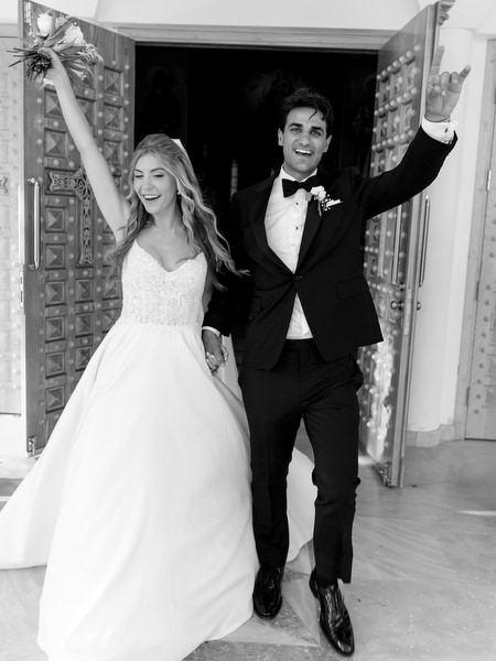 Bride and groom raising their arms as they exit Greek Orthodox church in Athens