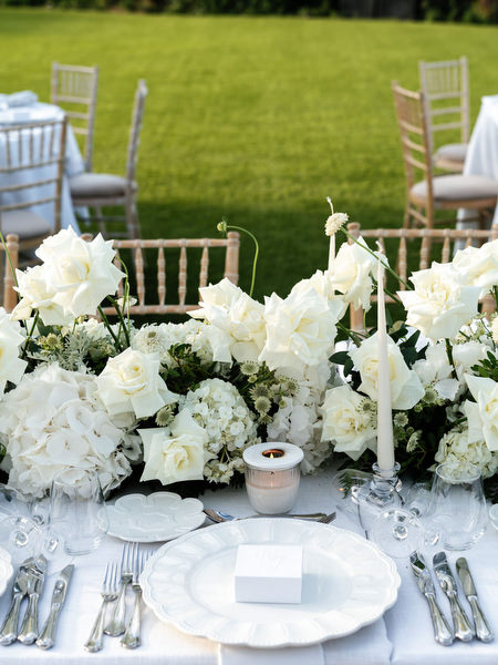 Elegant white place setting with layered white florals and taper candles at Athens Riviera wedding reception