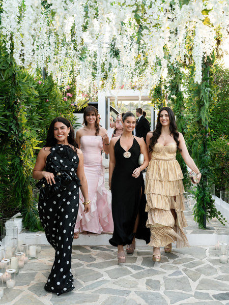 Female guests in formal gowns walking beneath hanging white florals at Island Resort Athens Riviera