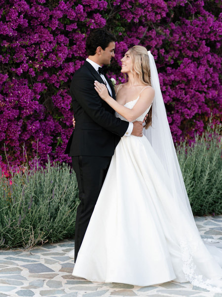 Bride and groom kissing in front of bright pink bougainvillea during Athens Riviera wedding portraits