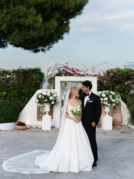 Bride and groom posing in front of white floral entrance arch at Island Resort Athens Riviera