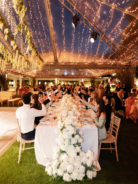 Long white floral banquet table beneath twinkling string lights at Island Resort Athens Riviera reception