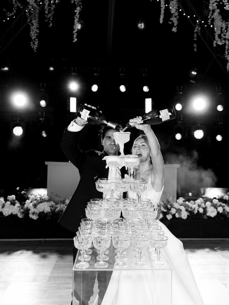 Bride and groom pouring champagne over tower in dramatic black and white reception portrait