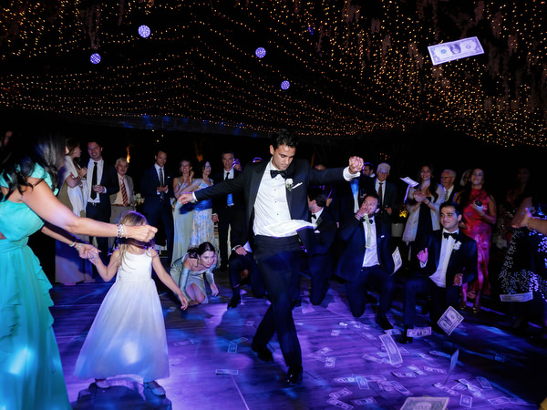 Groom dancing at center of circle of guests under string lights at Athens Riviera wedding reception