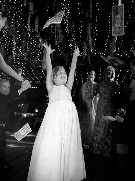 Flower girl on dance floor surrounded by scattered dollar bills during late-night Athens Riviera celebration