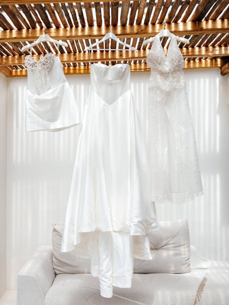 Three couture wedding dresses hanging beneath wooden pergola in sunlit Athens Riviera villa