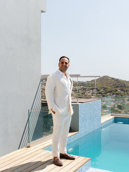 Groom in tailored white suit posing beside rooftop infinity pool in Athens