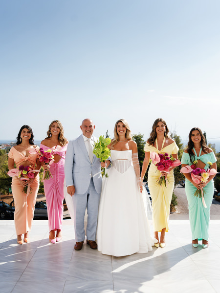 Bride walking with father and bridesmaids outside Athens church overlooking the sea