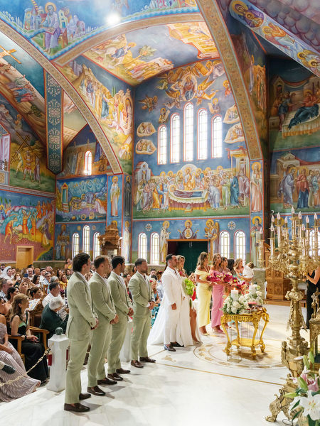 Bride and groom standing beneath ornate Byzantine frescoes during Athens church ceremony