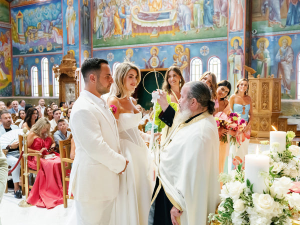 Priest blessing bride and groom beneath colorful Byzantine frescoes in Athens church