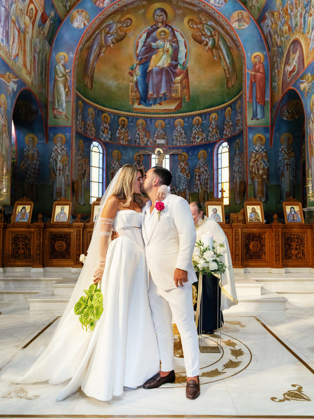 Bride and groom sharing a kiss beneath ornate dome during Athens wedding ceremony
