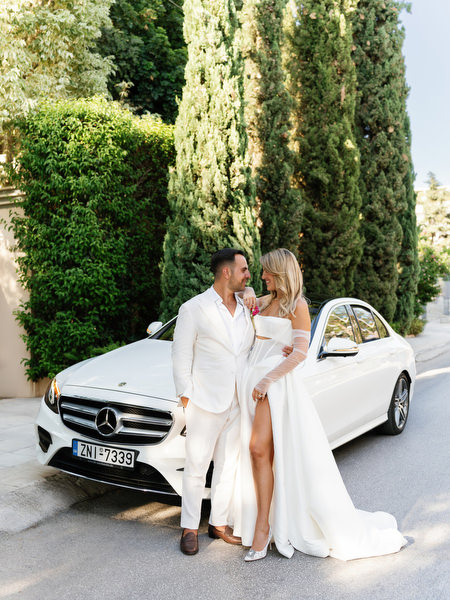 Bride and groom posing beside white luxury car after Athens church ceremony