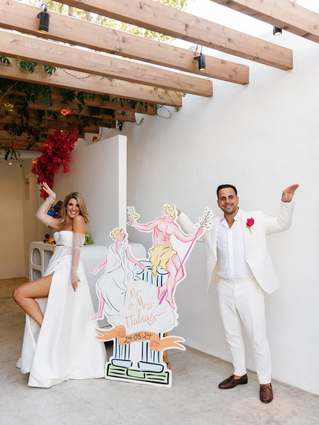 Bride and groom posing with custom Greco-Disco cutout installation at Athens Riviera celebration
