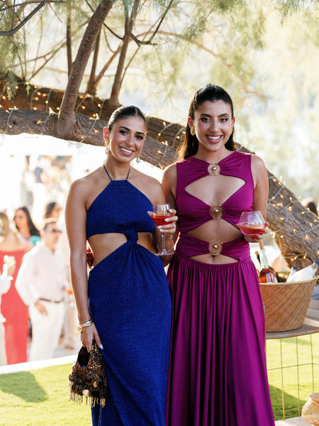 Wedding guests in bold blue and magenta gowns holding cocktails during Athens Riviera reception