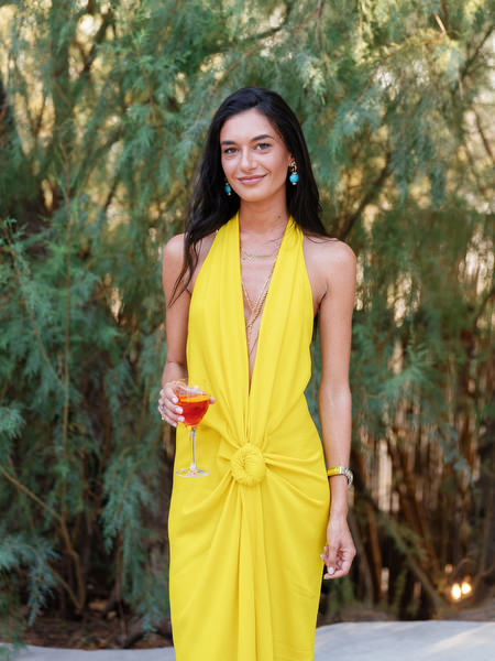 Wedding guest in bold yellow halter gown holding cocktail during Athens Riviera reception