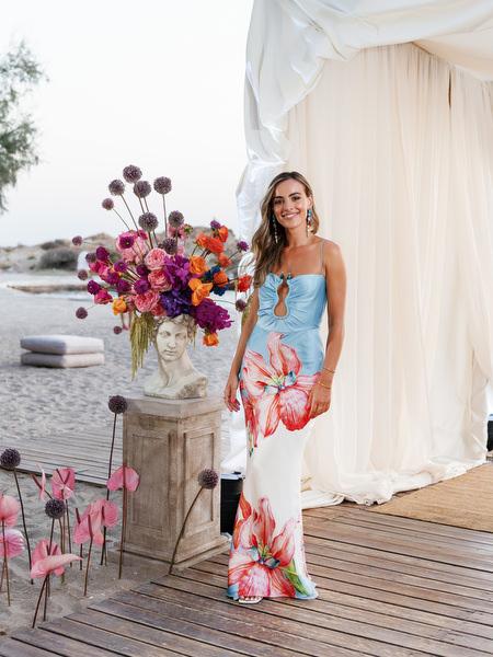 Guest in blue floral gown posing beside vibrant ceremony florals on the Athens Riviera