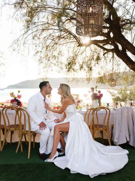 Bride and groom seated together at long seaside banquet table in Athens