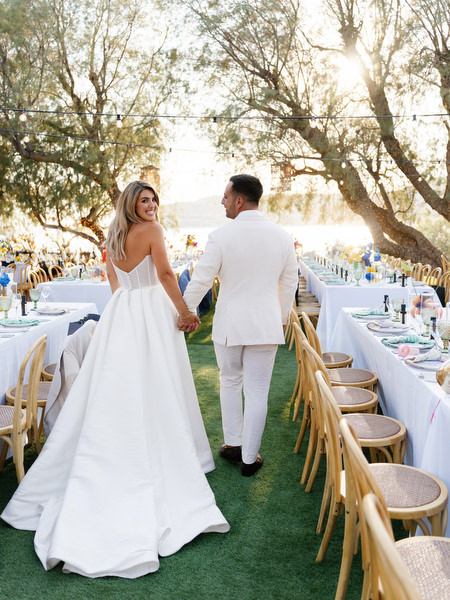 Bride and groom walking hand in hand between reception tables at Athens Riviera wedding