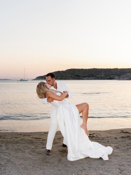 Groom dipping bride on the beach at sunset during Athens Riviera wedding