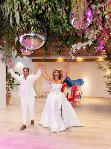 Bride and groom making a high-energy entrance into the Greco-Disco reception under hanging greenery and disco balls in Athens
