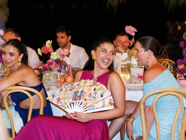 Wedding guest holding illustrated fan during colorful Athens Riviera reception dinner