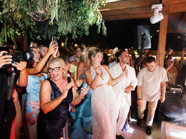 Bride and groom dancing in center of crowded wedding dance floor surrounded by cheering guests and photographers