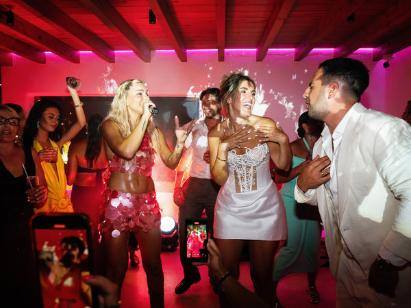 Bride in short reception dress singing and dancing with groom under pink party lighting