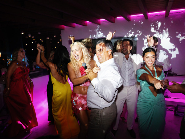Singer hugging guests while dancing on colorful wedding dance floor with editorial flash photography
