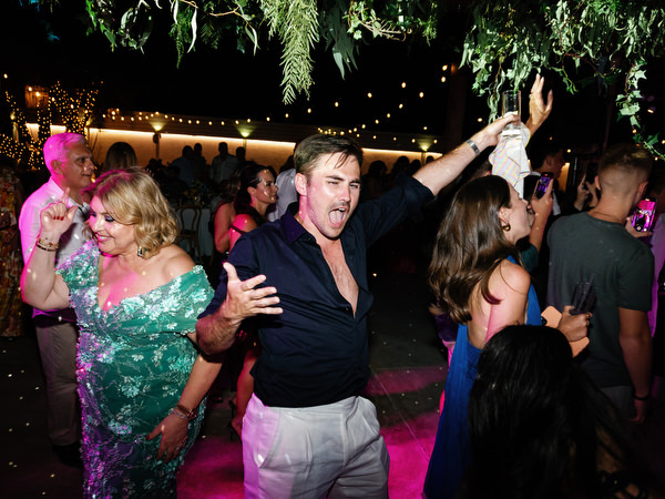 Wedding guests dancing outdoors under greenery and warm lights during lively late-night reception