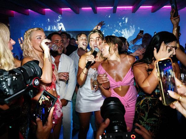 Bride and guests singing and celebrating while photographers capture high-energy wedding party scene