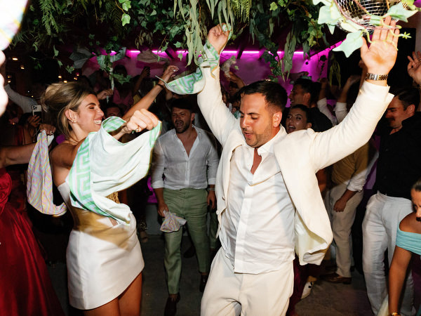 Bride and groom dancing with raised hands under hanging greenery and disco ball during vibrant reception