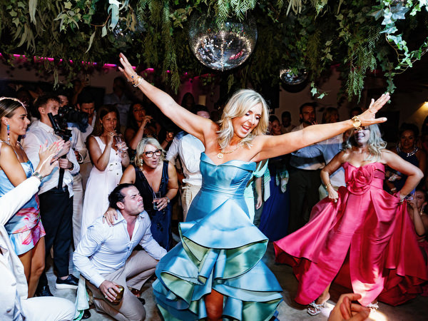 Female wedding guest in teal ruffled gown dancing confidently under disco ball during late-night celebration