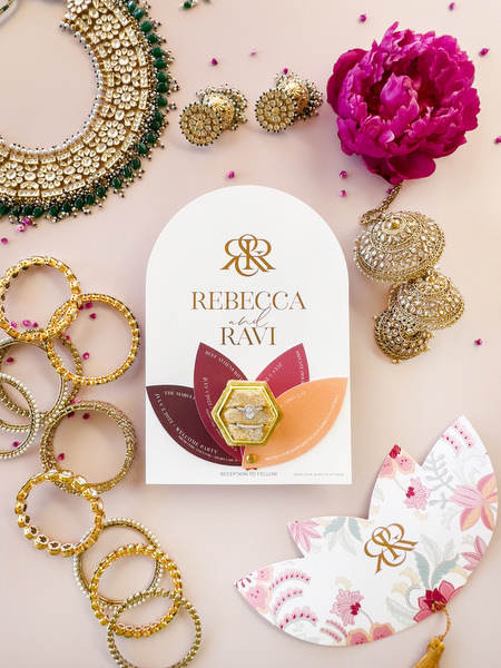 Rebecca and Ravi wedding invitation with gold monogram surrounded by Indian jewellery at Athens Riviera wedding.