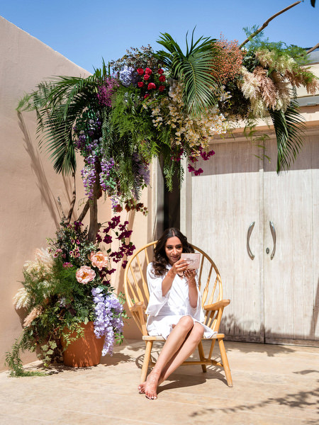 Bride seated in white robe beneath tropical wedding florals at Private House Island Resort Athens Riviera.