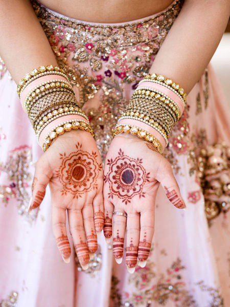 Bride showing detailed henna mehndi on hands wearing powder pink lehenga at Athens Riviera Indian wedding.