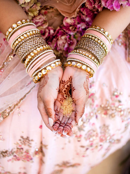 Bride holding grains during Hindu wedding ritual with intricate mehndi at Athens Riviera ceremony.