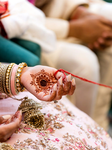 Close-up of bride’s henna hand holding sacred red thread during Indian wedding ceremony in Greece.