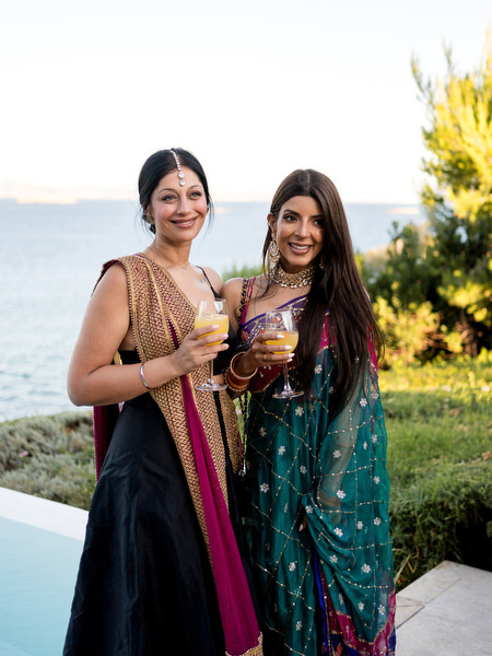 Two wedding guests in colourful saris holding cocktails at Private House Island Resort Athens Riviera Indian wedding.