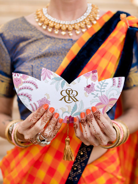 Close-up of guest holding Rebecca and Ravi monogram stationery in colourful sari at Athens Indian wedding.