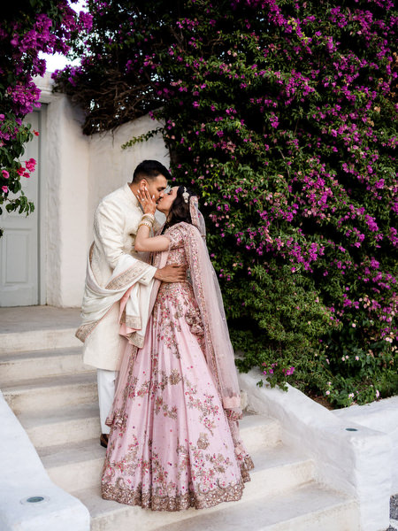 Bride and groom embracing beneath pink bougainvillea at Private House Island Resort Athens Riviera Indian wedding.