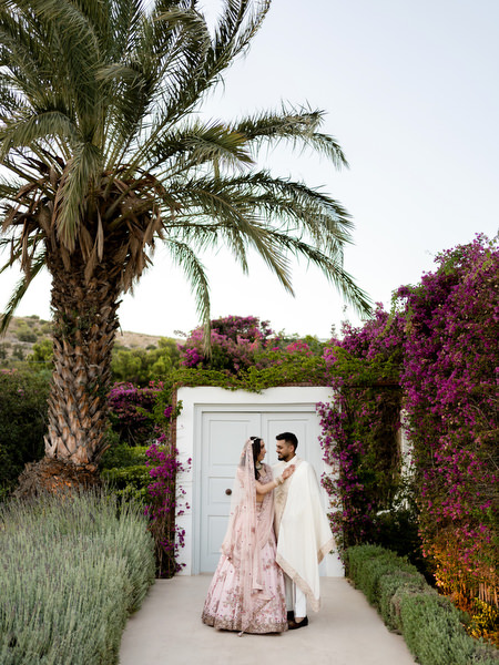 Bride and groom walking beneath palm trees and bougainvillea at Private House Island Resort Athens wedding.
